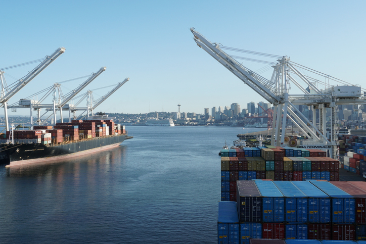 Seattle, USA 07 12 2021: Container SSA terminal with gantry cranes on both sides. There is a container merchant vessel being loaded and discharged on the left. Skyline of Seattle on the horizon.